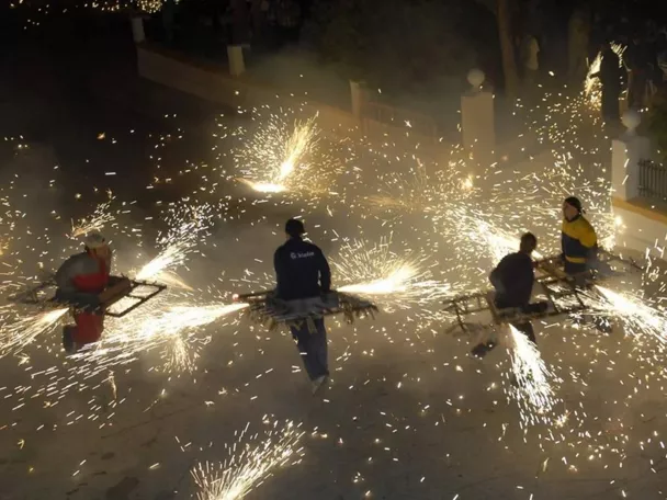 Personas portando estructuras con fuegos artificiales que lanzan chispas.