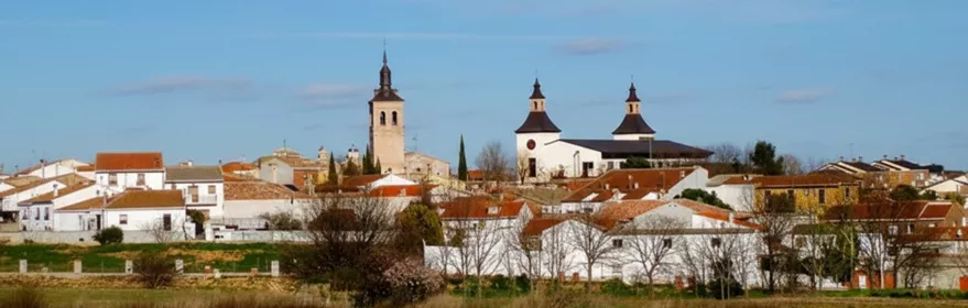Panorámica de un pueblo con casas blancas y tejados rojos desde un campo de vegetación seca.