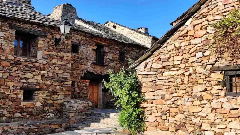 Fachadas de piedra con puertas de madera y vegetación entre muros.