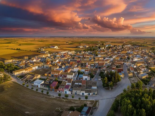 Vista aérea de Hoya Gonzalo al atardecer, rodeada de campos de cultivo bajo un cielo de tonos anaranjados y nubes espectaculares.