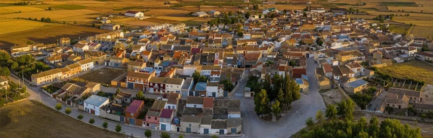 Vista aérea de Hoya Gonzalo al atardecer, rodeada de campos de cultivo bajo un cielo de tonos anaranjados y nubes espectaculares.