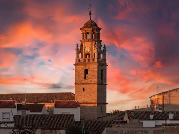 Torre de la iglesia de La Gineta destacando sobre los tejados del municipio durante un atardecer de tonos rosados.
