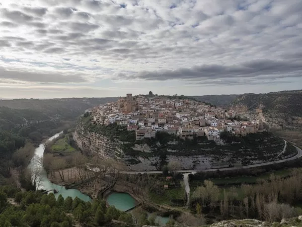 Vista aérea de Madrigueras asentada sobre un cerro junto al río Júcar, rodeada de paisaje natural y vegetación.