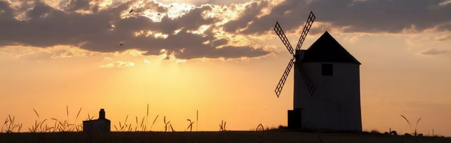 Molino de viento tradicional en Mahora recortado contra un cielo dorado al atardecer.