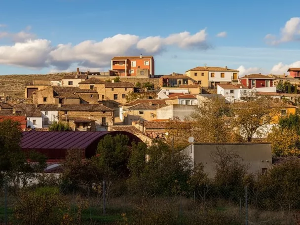 Vista del casco urbano de Masegoso con casas tradicionales sobre una colina bajo un cielo azul con nubes.
