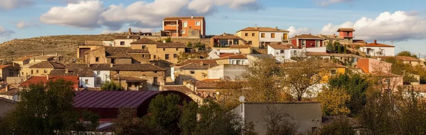 Vista del casco urbano de Masegoso con casas tradicionales sobre una colina bajo un cielo azul con nubes.