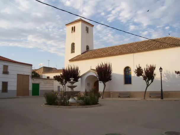 Iglesia de Montalvos con fachada blanca y torre cuadrada en una plaza tranquila con fuente central.