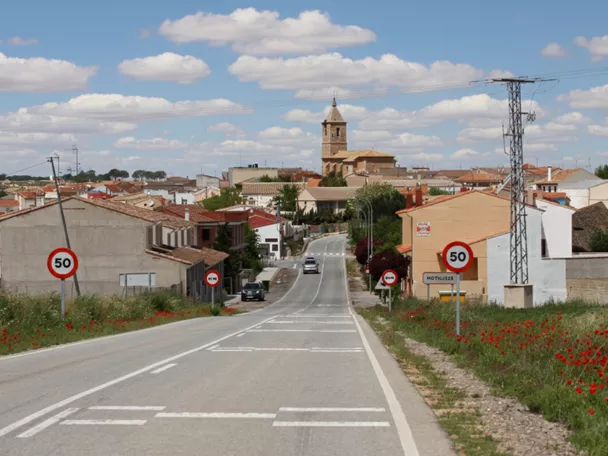 Carretera de acceso a Motilleja con vista del casco urbano y la torre de la iglesia al fondo.