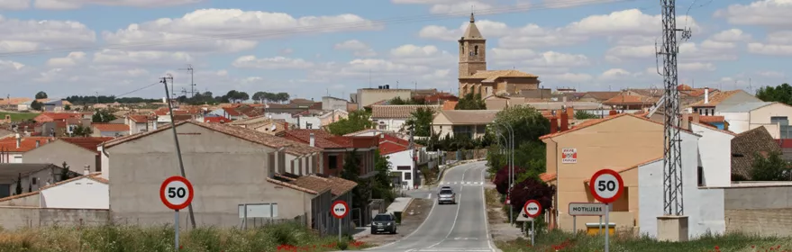 Carretera de acceso a Motilleja con vista del casco urbano y la torre de la iglesia al fondo.