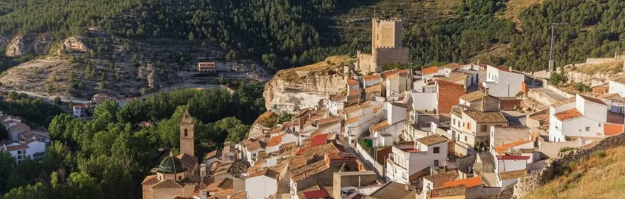 Vista aérea de Povedilla con casas blancas sobre la ladera y paisaje montañoso al fondo.