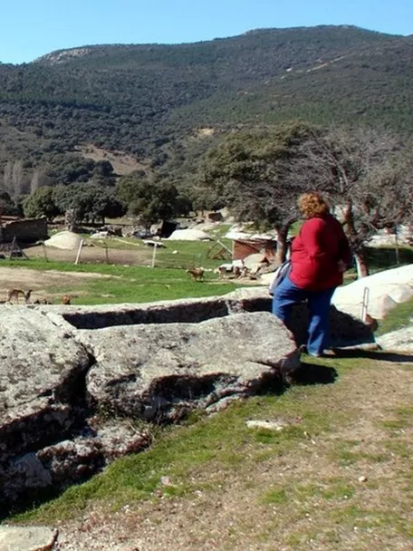 Tumbas excavadas en piedra con granja y torre al fondo.