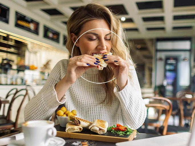 A beautiful mid adult blond woman, sitting in a cafe, she is enjoying her food and drinking coffee. There is a laptop in front of her, maybe she is taking a break from work.