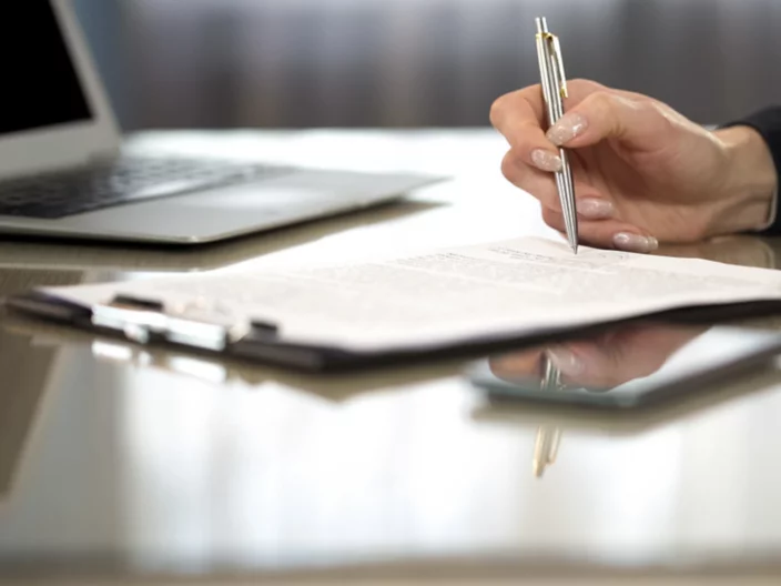 Woman in suit reading terms and conditions of agreement, signing contract