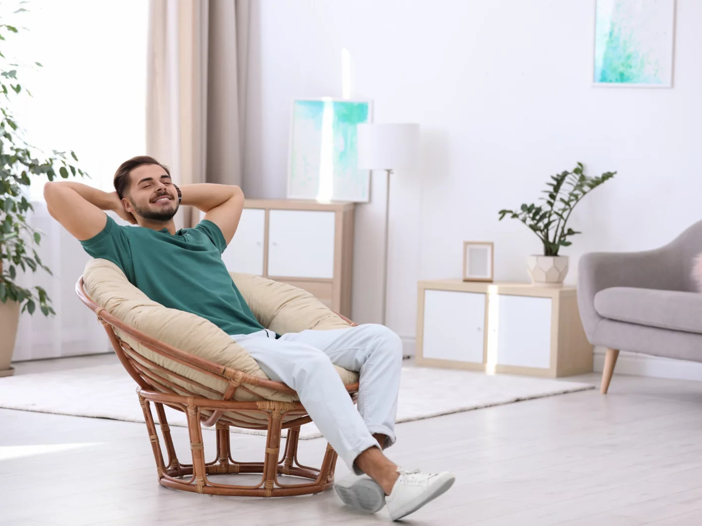 Handsome young man sitting in armchair at home. Space for text