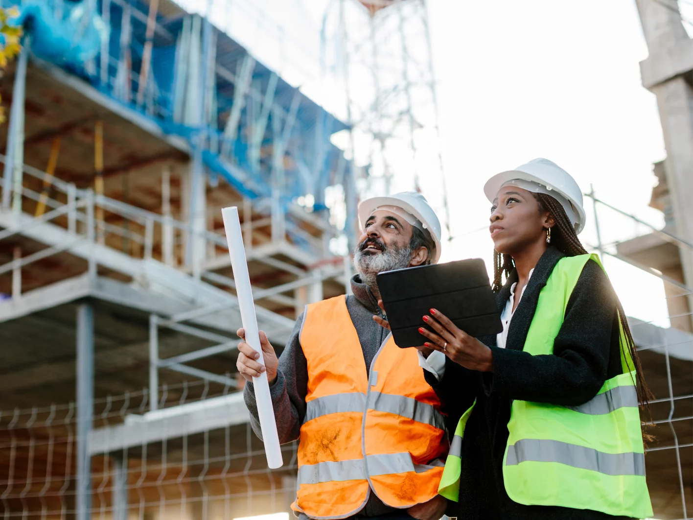 Woman engineer supervising construction of building with construction worker checking her tablet device