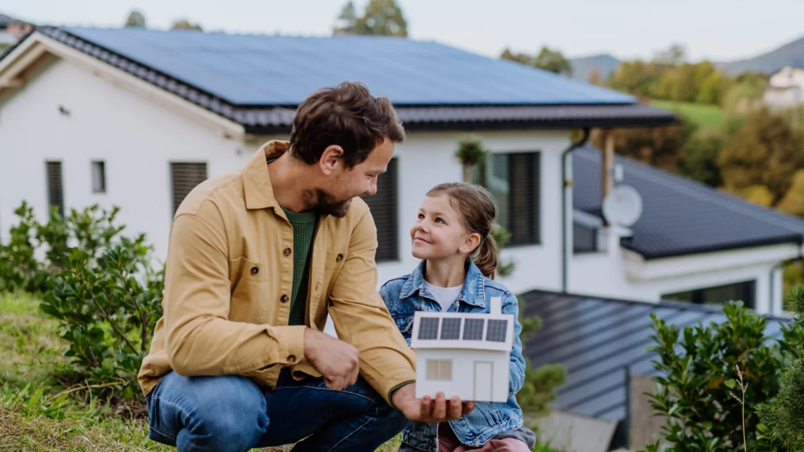 Little girl with her dad holding paper model of house with solar panels, explaining how it works.Alternative energy, saving resources and sustainable lifestyle concept.