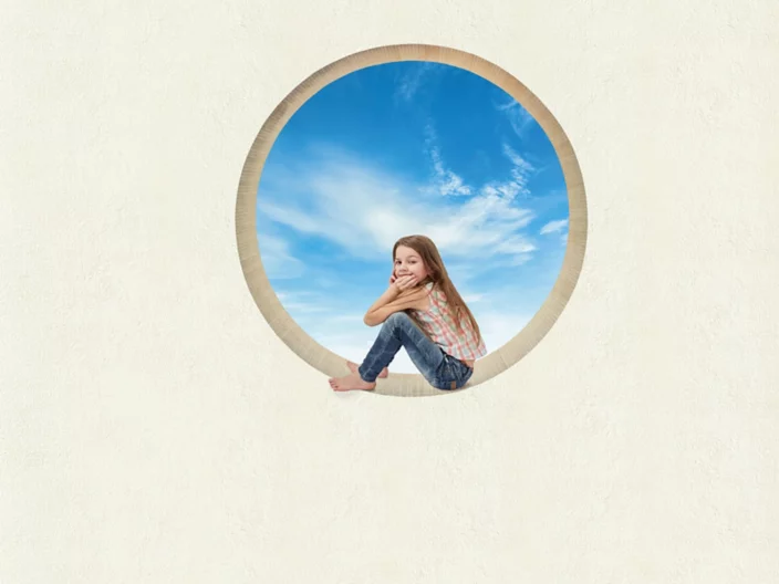 Kind sitzt in rundem Fenster vor blauem Himmel