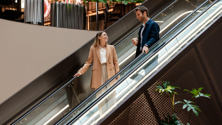 Une femme et un homme sur des escalators dans un centre commercial.