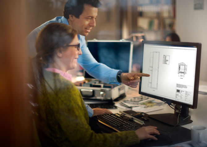 Two colleagues conversing in front of a computer screen.