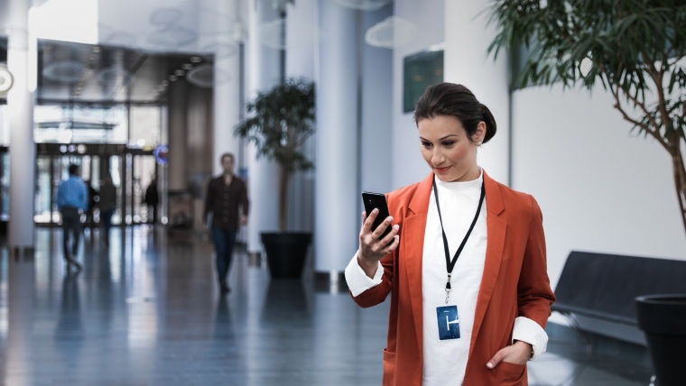 KONE - Woman looking at her phone in an office building lobby.
