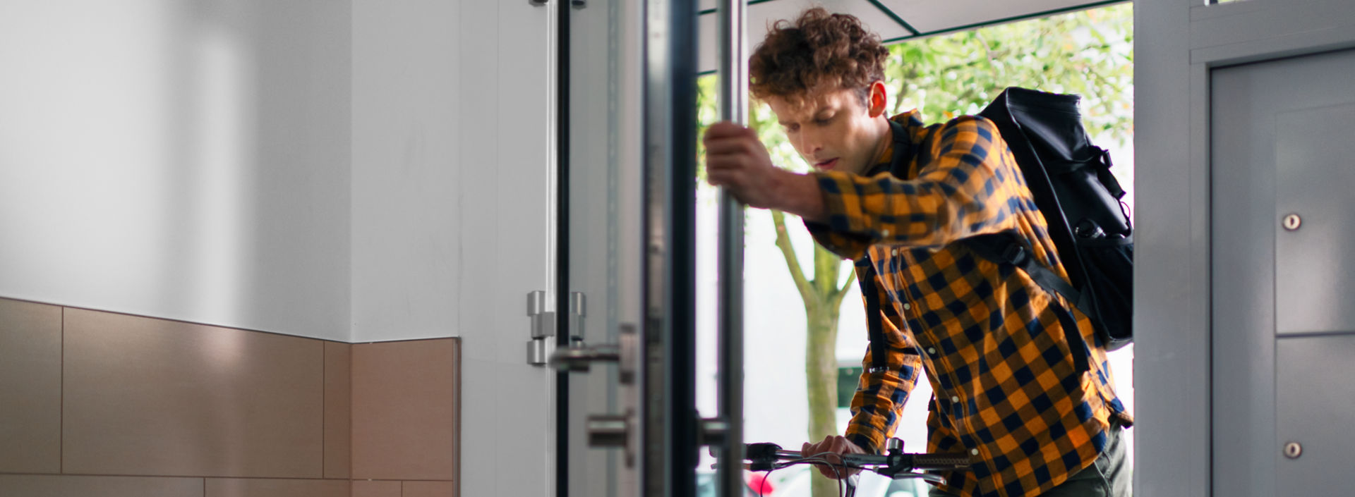 Cyclist_struggling_with_door_in_residential_building_1:1920x705%28hero%29