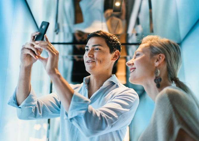 Two people taking pictures with a smartphone in an elevator.