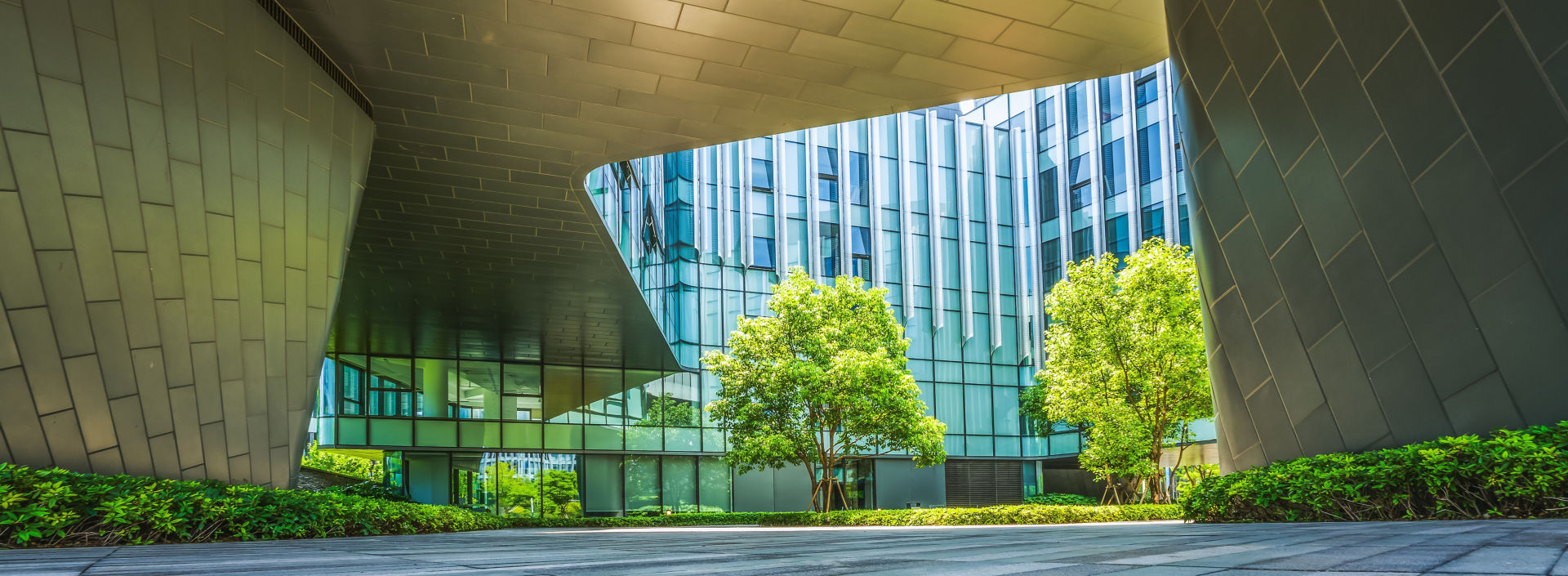 The outside of a concrete, wood and glass building with green trees.