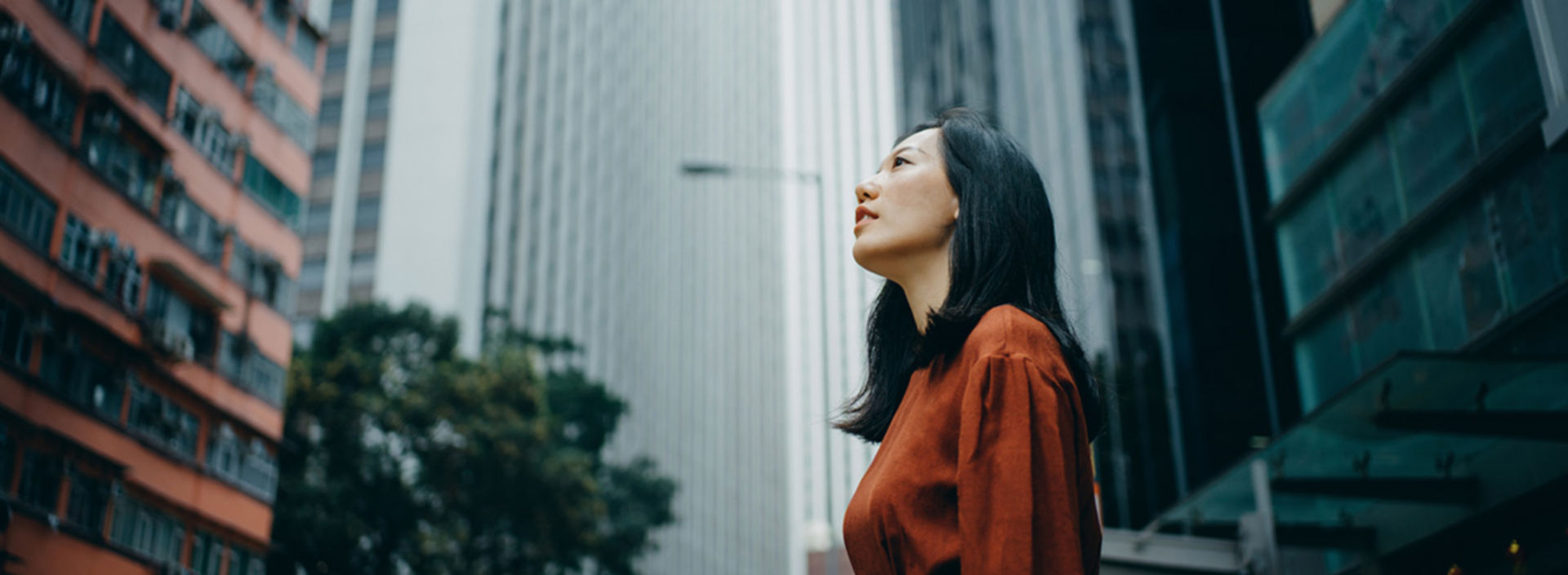 A woman in a red dress looks up at high-rise buildings.