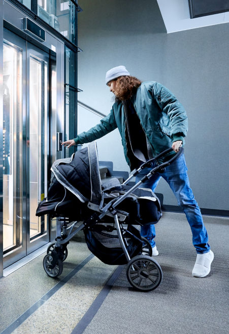 Man with a baby stroller pushing an elevator call button in a residential stairway