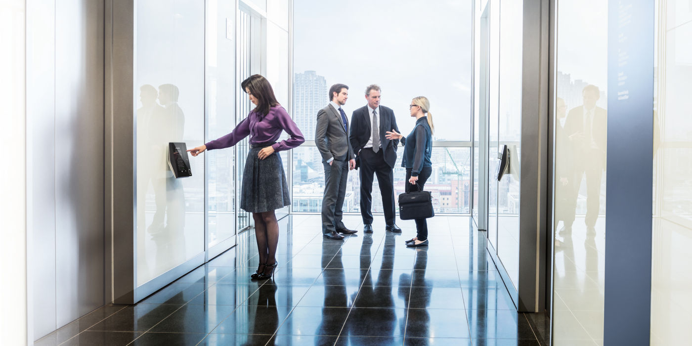 Grupo de personas de negocios dentro de edificio y una mujer pidiendo un elevador - KONE Destination
