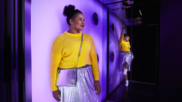 Woman is standing in an elevator and her reflection in the mirror is dancing.