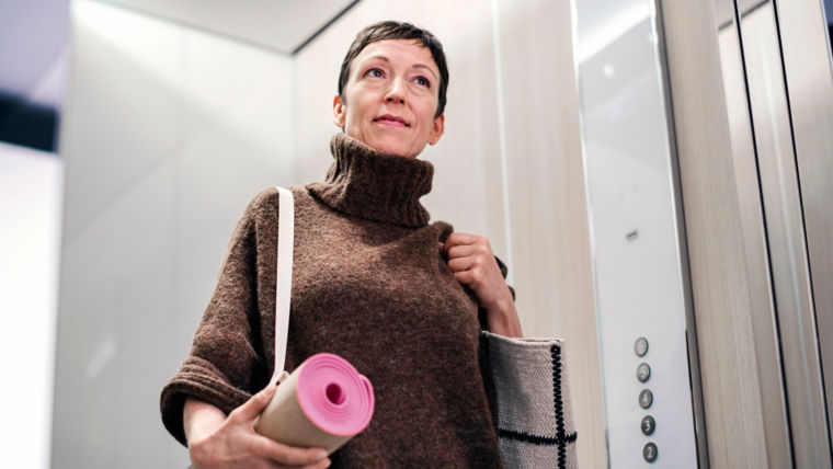 Woman in elevator carrying yoga mat.