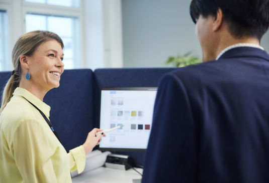 Two colleagues conversing in front of computer screen.