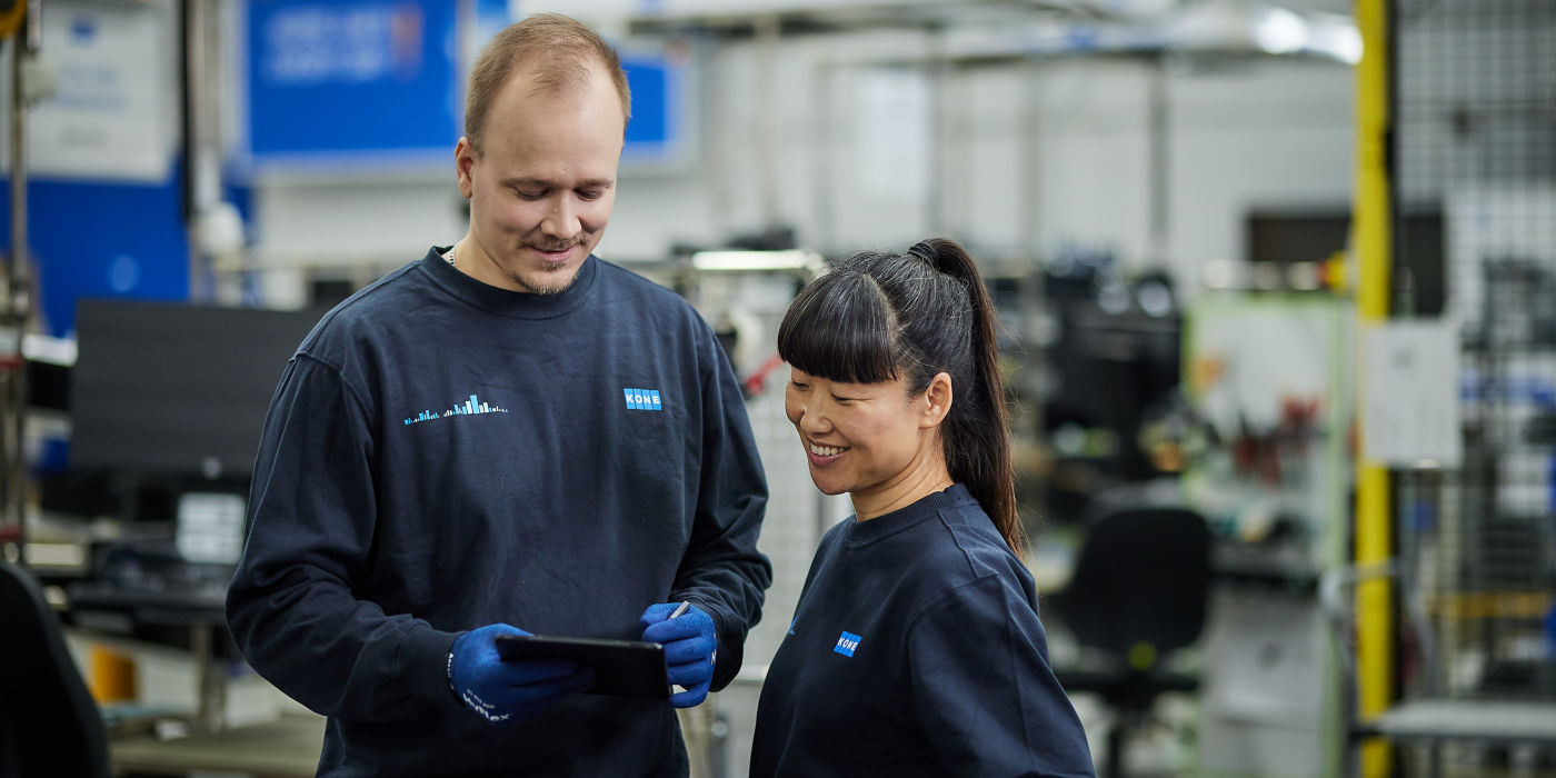 Two KONE employees looking at tablet in factory.