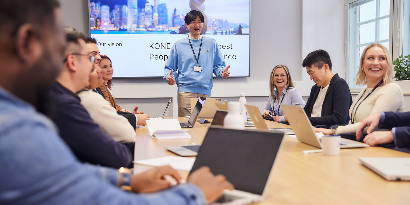 Group of smiling KONE employees sitting at their computers in meeting room.