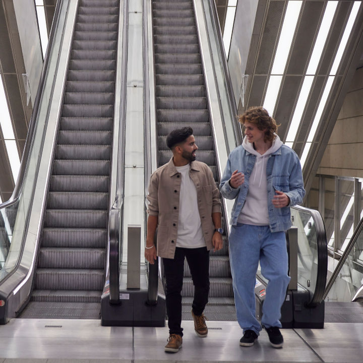 Two men walking from an escalator while having a conversation.