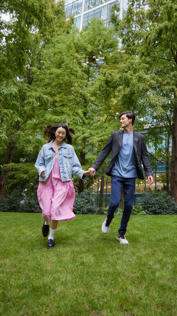 Happy Asian couple running in the park next to a high-rise building