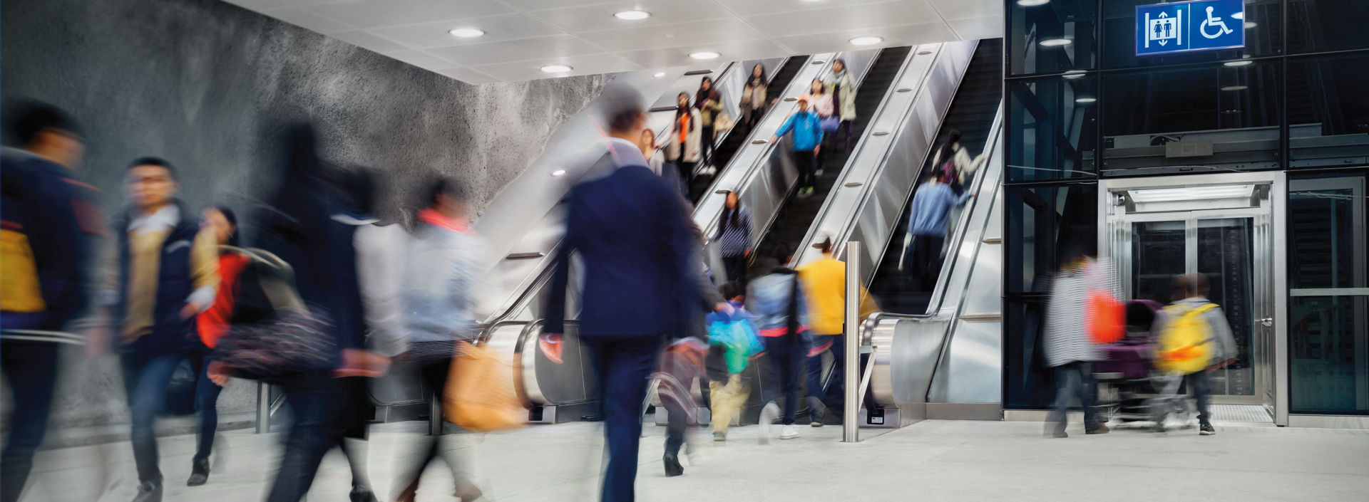 People walking and taking escalators and elevator at a busy metro station.