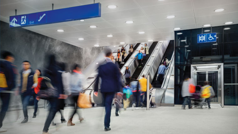 People walking and taking escalators and elevator at a busy metro station.