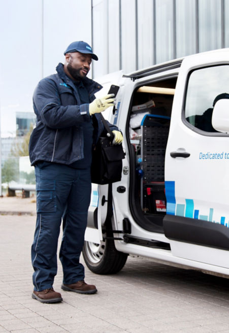 KONE maintenance worker looking at his phone next to KONE maintenance van.
