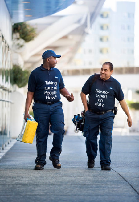 Two KONE maintenance workers walking next to a office building while conversing.