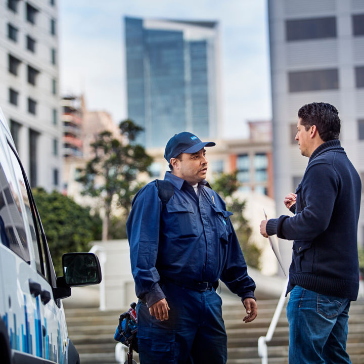 KONE maintenance service worker conversing with client outside next to KONE maintenance van.