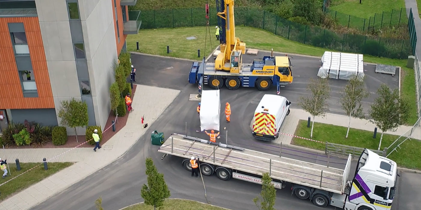 Crane offloads a large package from a truck on a parking lot of a residential building.