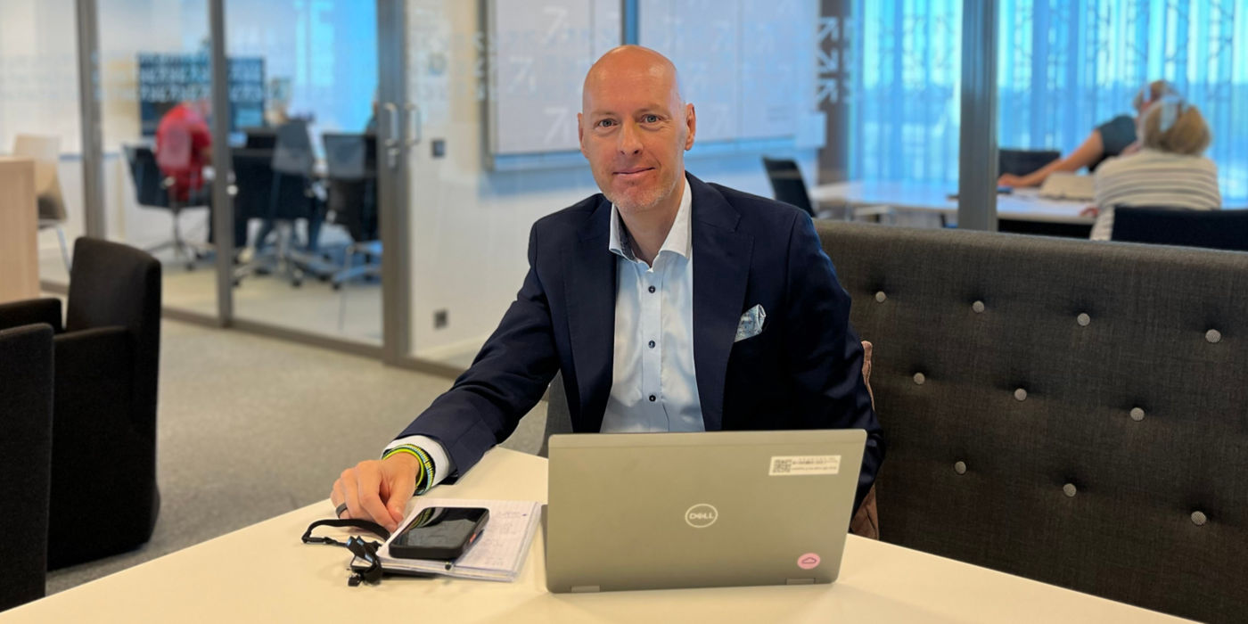 Petteri Rantanen in KONE meeting room, with colleagues discussing in glass wall rooms in the background.