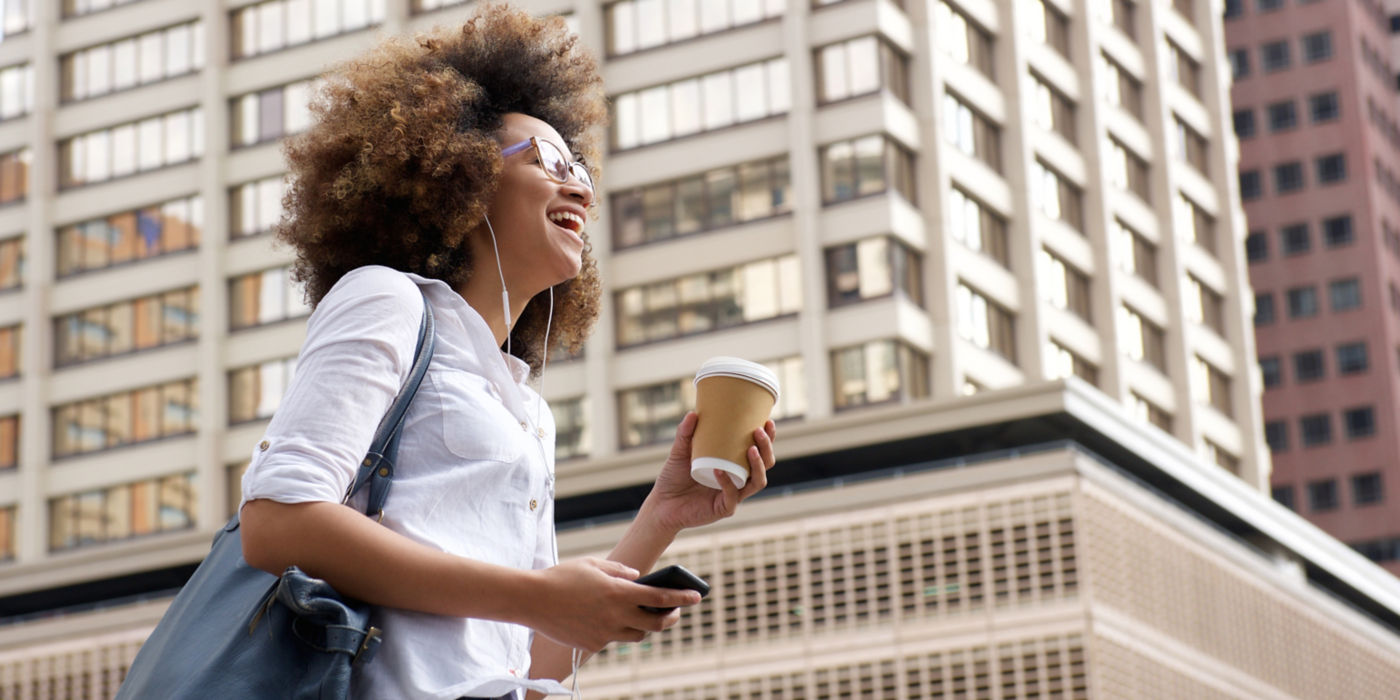 Side portrait of a smiling african american woman walking in the city with cellphone.