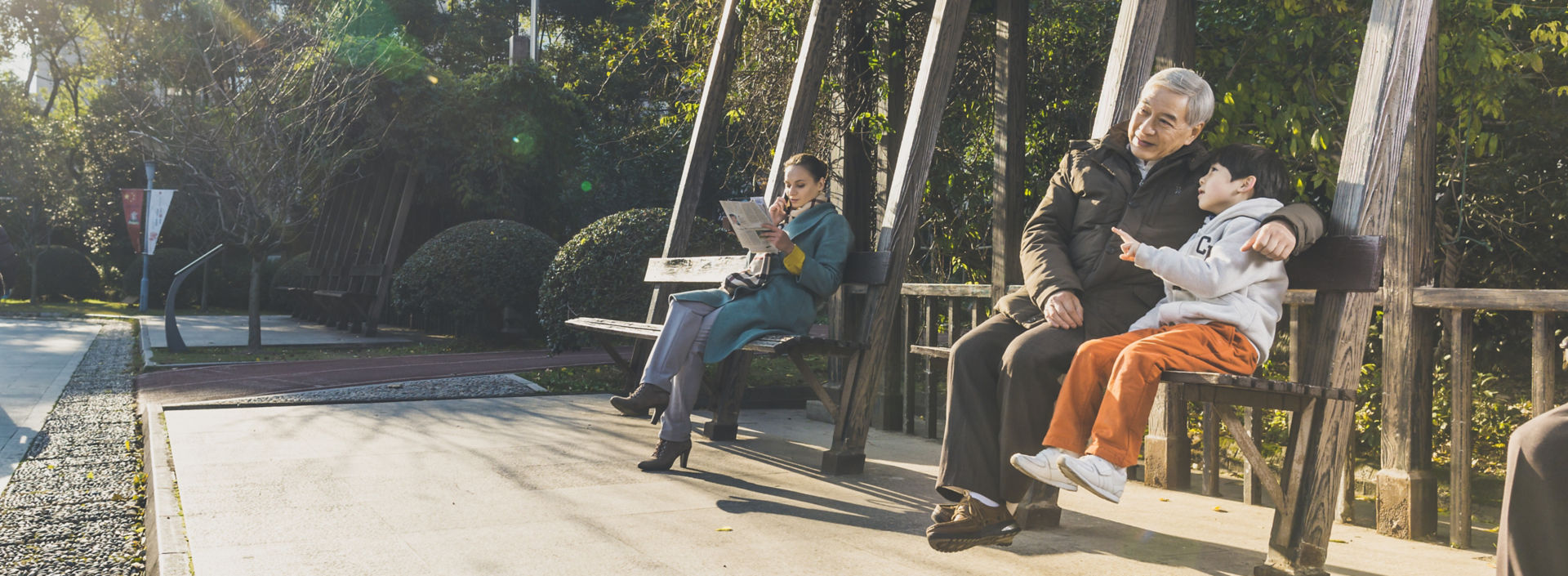 A young boy and elderly man sit on a bench among green trees in China.