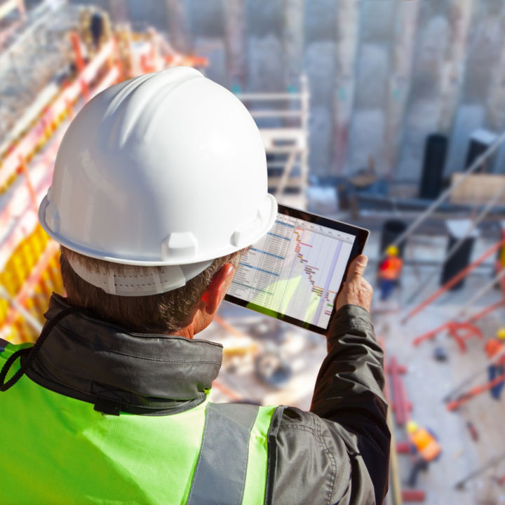 Manager with hardhat on construction site checking schedule on tablet.
