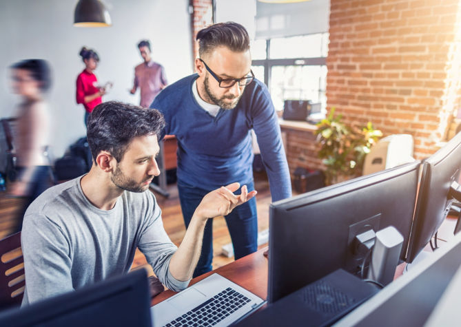 Two colleagues collaborating at an office in front of a computer.