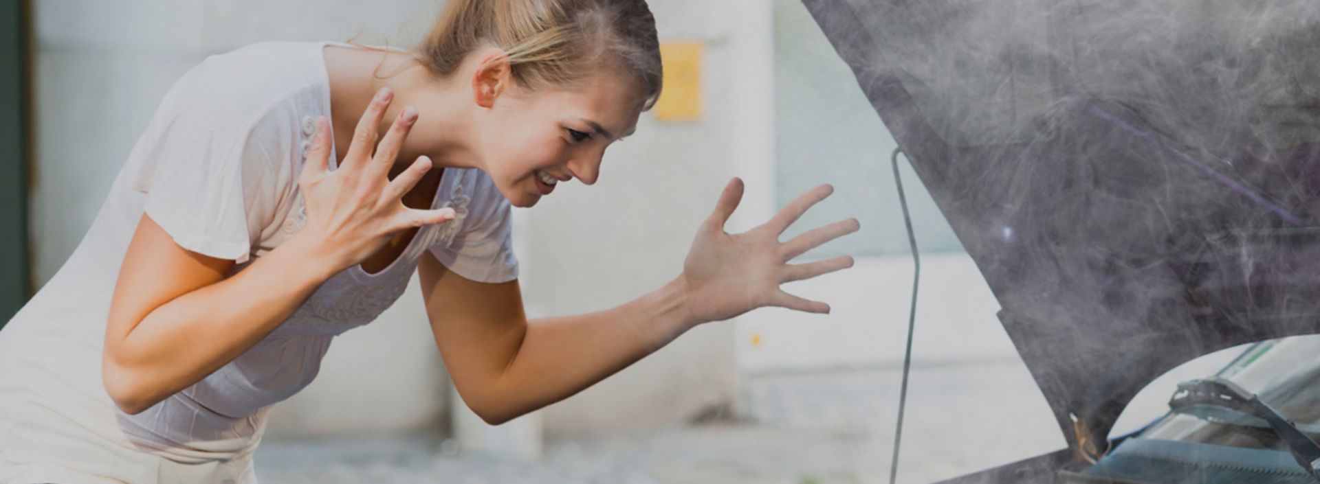 Mujer desesperada abriendo el cofre de automóvil con humo - KONE Moderniza tu elevador