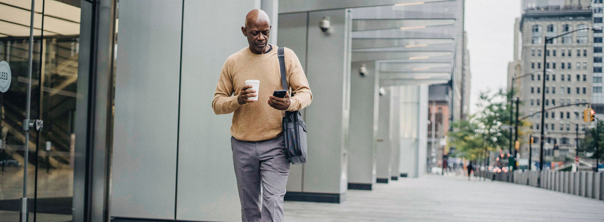 KONE - Man walking outside office building holding coffee cup and a smartphone.